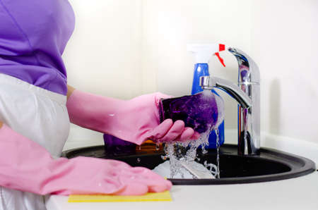 Woman rinsing plates under running water the tap as she does the washing up after a meal, close up of her gloved handsの写真素材