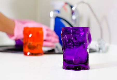 Woman wiping the kitchen counter top with a dishcloth as she places the clean glasses and crockery from washing up on the surfaceの写真素材