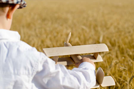 Cute little boy flying his toy plane in a wheat field standing in the ripening golden ears of wheat...