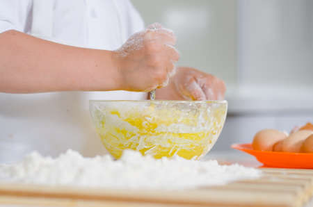 Little boy mixing cake ingredients in a mixing bowl whipping the flour and eggs to make the doughの写真素材