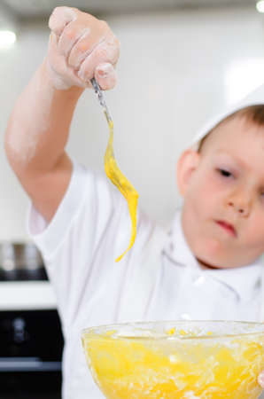 Cute young boy learning to bale a cake carefully watching fresh beaten eggs dripping off the fork into his mixing bowlの写真素材