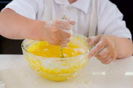 Little boy mixing cake ingredients in a mixing bowl whipping the flour and eggs to make the doughの写真素材