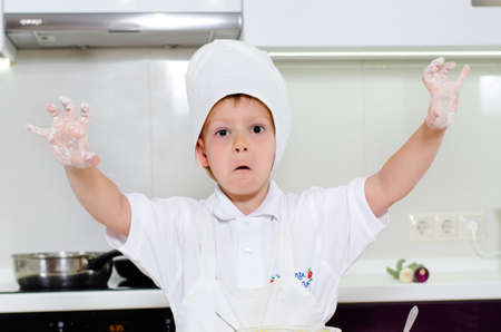 Laughing young boy with floury hands showing them to the camera as he stands in the kitchen learning to bakeの写真素材