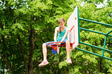 Young girl sitting in hoop in an outdoor basketball courtの写真素材
