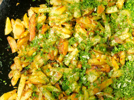 Delicious freshly cut potato chips and chopped herbs cooking in oil on a BBQ on a summer picnic,...