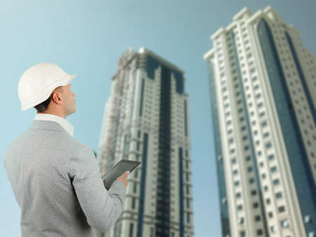 Building inspector or structural engineer wearing a hardhat standing with a tablet computer surveying a newly built office block in a conceptual imageの写真素材