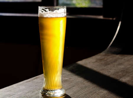 Ice Cold Beer on Classic Tall Glass Placed on Vintage Wooden Table Near the Window at the Bar.