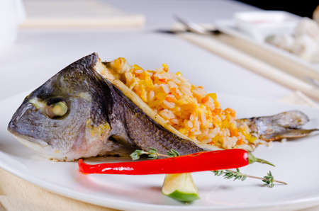 Close up side view of a whole grilled fish stuffed with savory spicy rice and served with lime and chili pepper for a gourmet seafood mealの写真素材