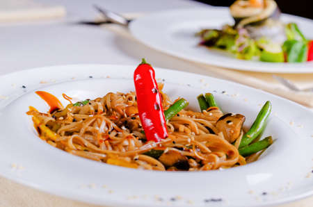 Close up Red Chili Pepper and Green Bean Cuts on Savory Noodles Recipe. Prepared on White Round Plate at the Restaurant Table.の写真素材