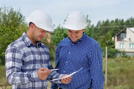 Architect and engineer having a discussion referring to a paper document as they stand on a building...