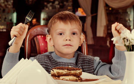 Little boy waiting to tuck into his dessert at the dining table holding his fork poised over a delicious slice of fresh tart or cakeの写真素材