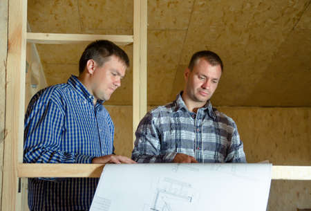Two builders discussing a building plan as they stand in the interior of a new build timber frame house still under constructionの写真素材