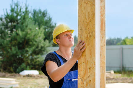 Builder installing wall insulation holding upright a wooden insulated polystyrene beam in a vertical...