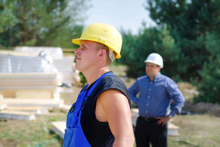 Builder and architect standing watching something off frame to the left on a building site with the workman in the foregroundの写真素材