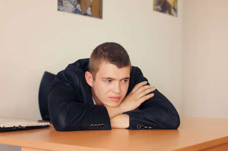 Young Businessman Resting Head on Desk and Looking Optimisticの写真素材