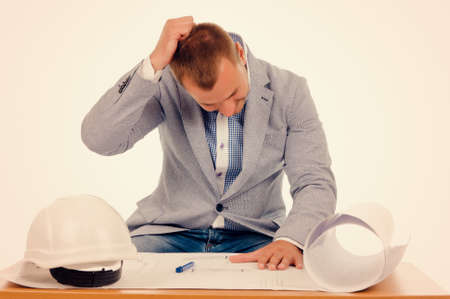 Close up Shot of Worried Male Project Designer Scratching his Head While Looking at Blueprint on the Table. Isolated on Off White Background.の写真素材