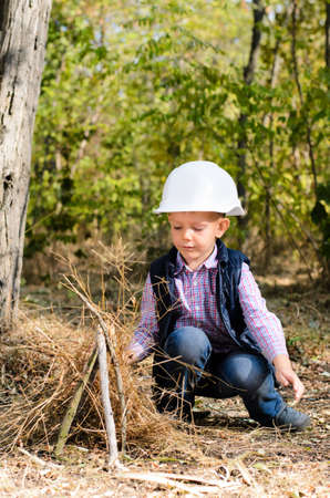 Close up Cute Little Boy in Autumn Outfit Playing with Sticks on the Ground at the Woodlandの写真素材