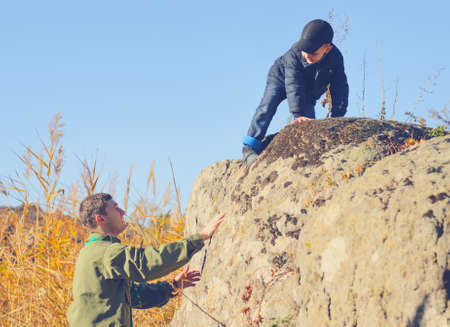 Scout helping a young boy rock climbing giving him a helping hand from below as he learns about the wilderness and natureの写真素材