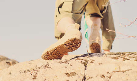 Close up Brown Shoes of a Boy Scout Climbing at the Huge Rock with Light Blue Sky Background.の写真素材