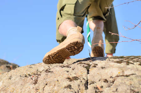 Close up Brown Shoes of a Boy Scout Climbing at the Huge Rock with Light Blue Sky Background.の写真素材