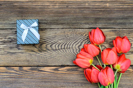 Bouquet of fresh colorful red tulips with a decorative gift lying on a rustic wooden background symbolic of an anniversary, Valentines Day and love, overhead viewの写真素材