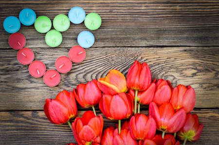 Bunch of fresh red tulips lying alongside a a heart formed of colorful candles for a loved one or sweetheart on Valentines Day or an anniversary, overhead viewの写真素材