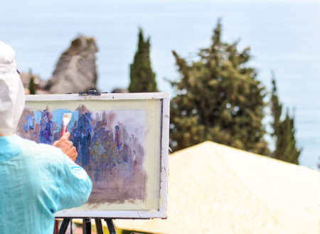 Skilled artist painting nature with brush on easel, outdoors, inspired by a scenic landscape with tall green trees, shot from rearの写真素材