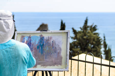 Rear View of Head and Shoulders of Woman Painting Scenic Outdoor View on Canvas Overlooking Coastの写真素材