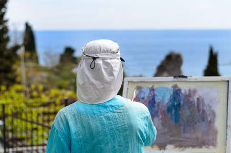 Rear View of Head and Shoulders of Woman Painting Scenic Outdoor View on Canvas Overlooking Coastの写真素材