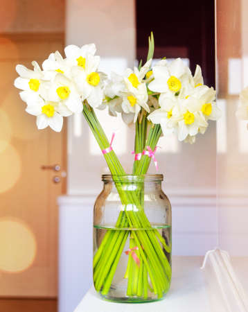 Glass jar with filled with pretty fresh white daffodils symbolic of springtime and the spring seasonの写真素材