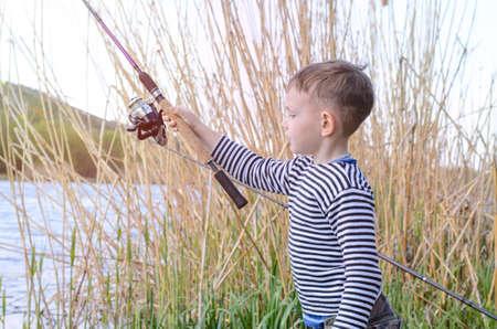 Handsome Young Kid at the Grassy Riverside, Holding his Fishing Rod While Looking at the Camera.の写真素材