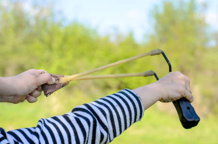 Close Up Side View of Boy Wearing Striped Shirt Holding Sling Shot with Rubber Bands Pulled Back in Anticipation of Catapulting Projectileの写真素材