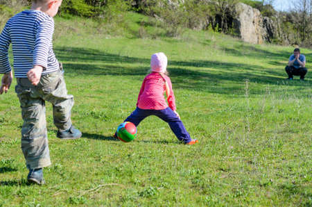 Young Brother and Sister Siblings Kicking Colorful Soccer Ball Together in Grassy Field on Sunny Day