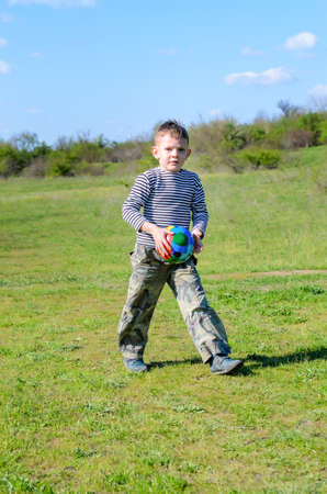 Full Length of Young Boy Walking Through Grassy Field and Carrying Colorful Ball While Looking at Cameraの写真素材