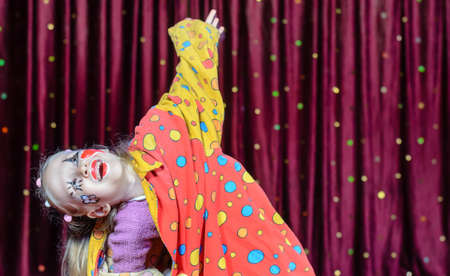 Young Blond Girl Wearing Clown Make Up and Polka Dot Costume Shielding Eyes from Bright Stage Lights in front of Red Curtainの写真素材