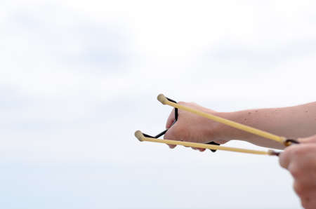 Close up Human Hand Pulling Bands of his Stone Shooter Stick Against White and Blue Sky.の写真素材