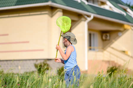 Little boy catching insects with a net in the long spring grass outside his house on a sunny dayの写真素材