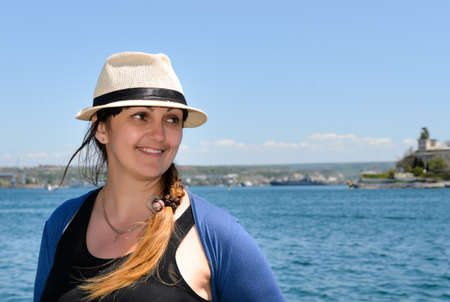 Smiling trendy woman wearing a chic hat with her long hair in a braid enjoying a sunny day at the...