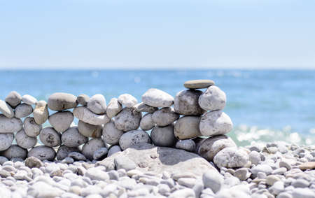 Stones stacked into a wall at the seaside on a beach strewn with pebbles against a tropical ocean backdropの写真素材