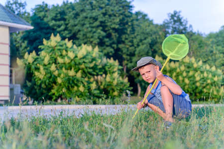 Portrait of Serious Young Boy with Bug Net Crouching in Long Grass on Lawn Outdoors in Summer
