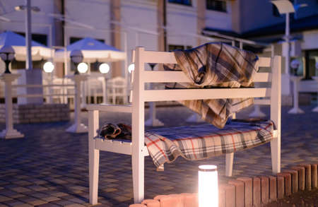 Inviting White Bench Covered in Plaid Blankets on Stone Patio Illuminated in Soft Light at Duskの写真素材