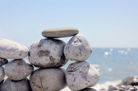Small Flat Rock Balancing on Top of Small Rock Wall on Beach with Sparkling Ocean Water in Backgroundの写真素材