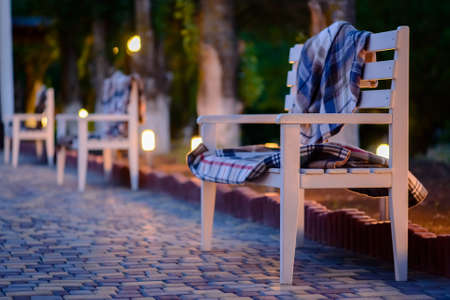 Blankets Piled on Empty Wooden Bench, Row of Benches on Stone Patio in Cozy Outdoor Setting Lit by Soft Evening Lightの写真素材