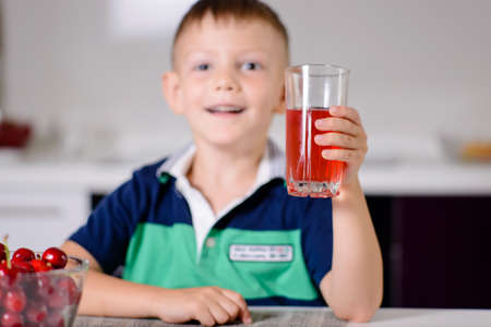 Thirsty little boy drinking fruit juice in a kitchen peering over the top of the glass with a serious expressionの写真素材