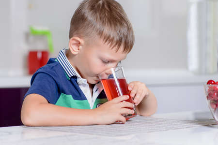 Thirsty little boy drinking fruit juice in a kitchen peering over the top of the glass with a serious expressionの写真素材