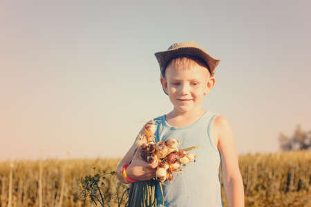 Close up Cute Young White Boy Eating and Holding Fresh Green Onions at the Farmの写真素材