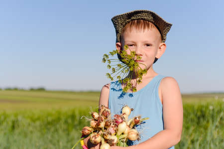 Close up Cute Young White Boy Eating and Holding Fresh Green Onions at the Farmの写真素材