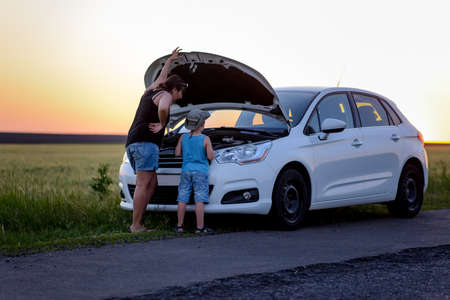 Rear View of a Mother and Son Repairing Something on their White Car at the Grassy Street Side on One Afternoon.の写真素材