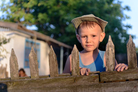 Portrait of a Cute Young Boy with Cowboy Hat Holding at the Wooden Fence, Smiling at the Cameraの写真素材
