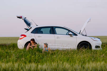 Mom and Son Sitting Beside their White Defective Car While Waiting for a Mechanicの写真素材